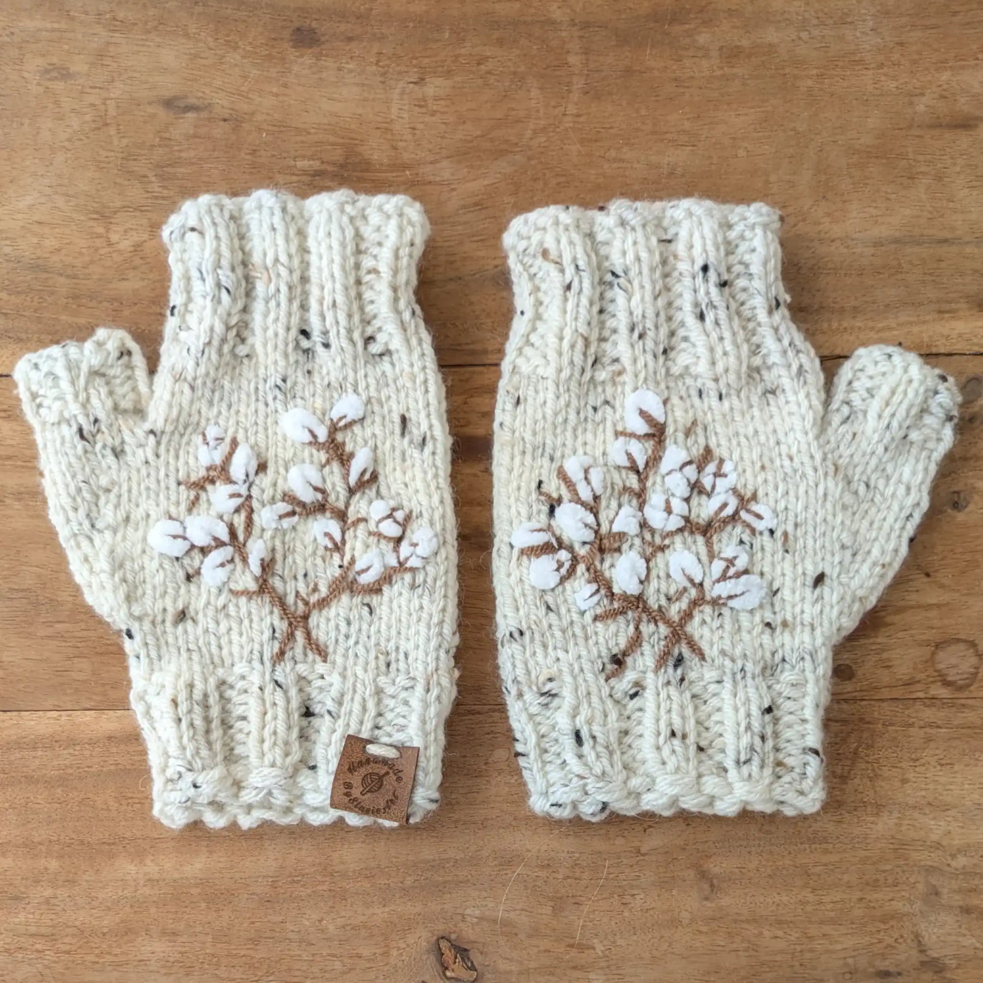 Mitaines écru moucheté faites main, avec broderies brunes en forme de branches de coton. Posées à plat.