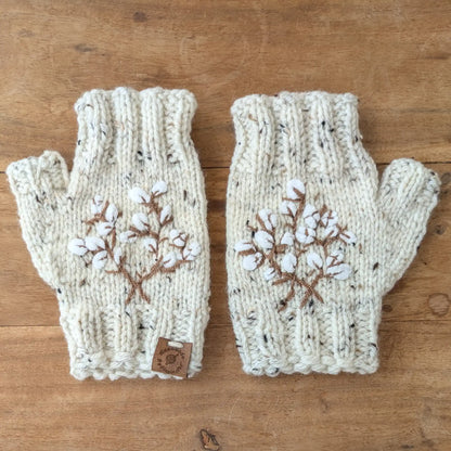 Mitaines écru moucheté faites main, avec broderies brunes en forme de branches de coton. Posées à plat.