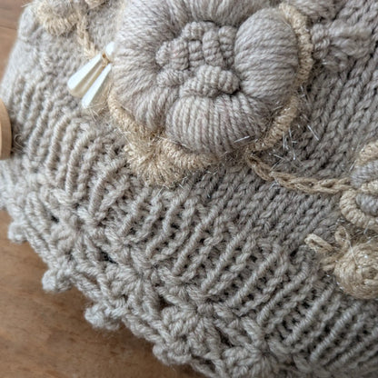Gros plan sur les fleurs écrues en relief et les perles translucides cousues sur les mitaines gris clair.