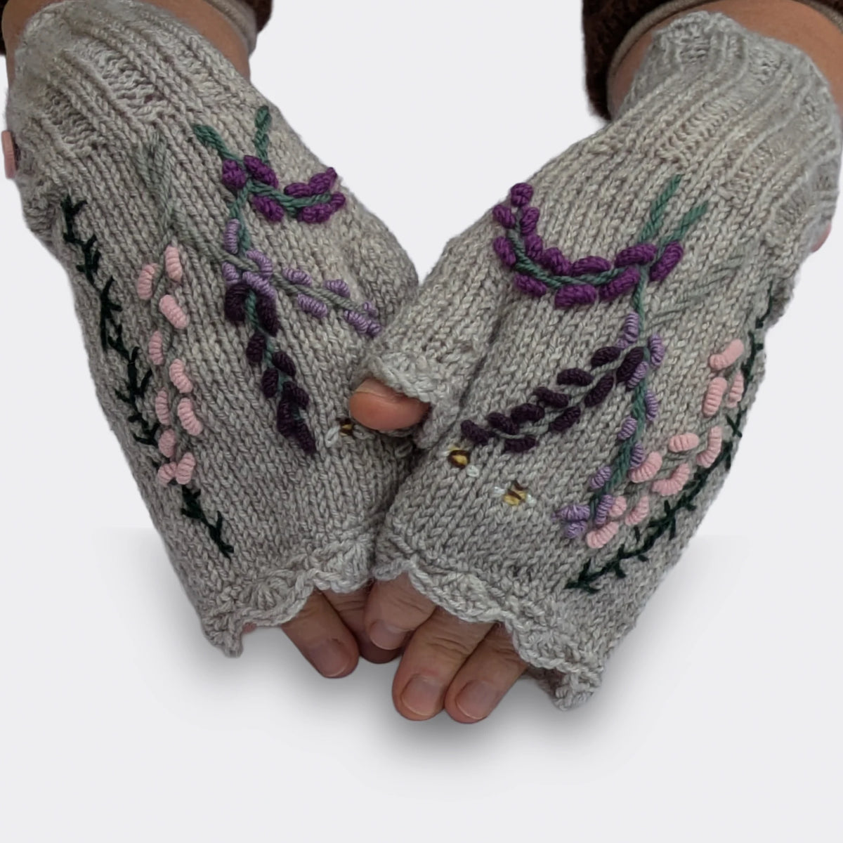 Mitaines pour femme grises portées sur des mains légèrement croisées. Le décor représente des fleurs parme et violettes sur des tiges élancées, ainsi que deux abeilles parmi les feuillages.