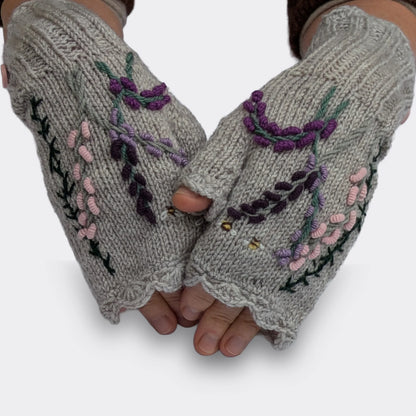 Mitaines pour femme grises portées sur des mains légèrement croisées. Le décor représente des fleurs parme et violettes sur des tiges élancées, ainsi que deux abeilles parmi les feuillages.