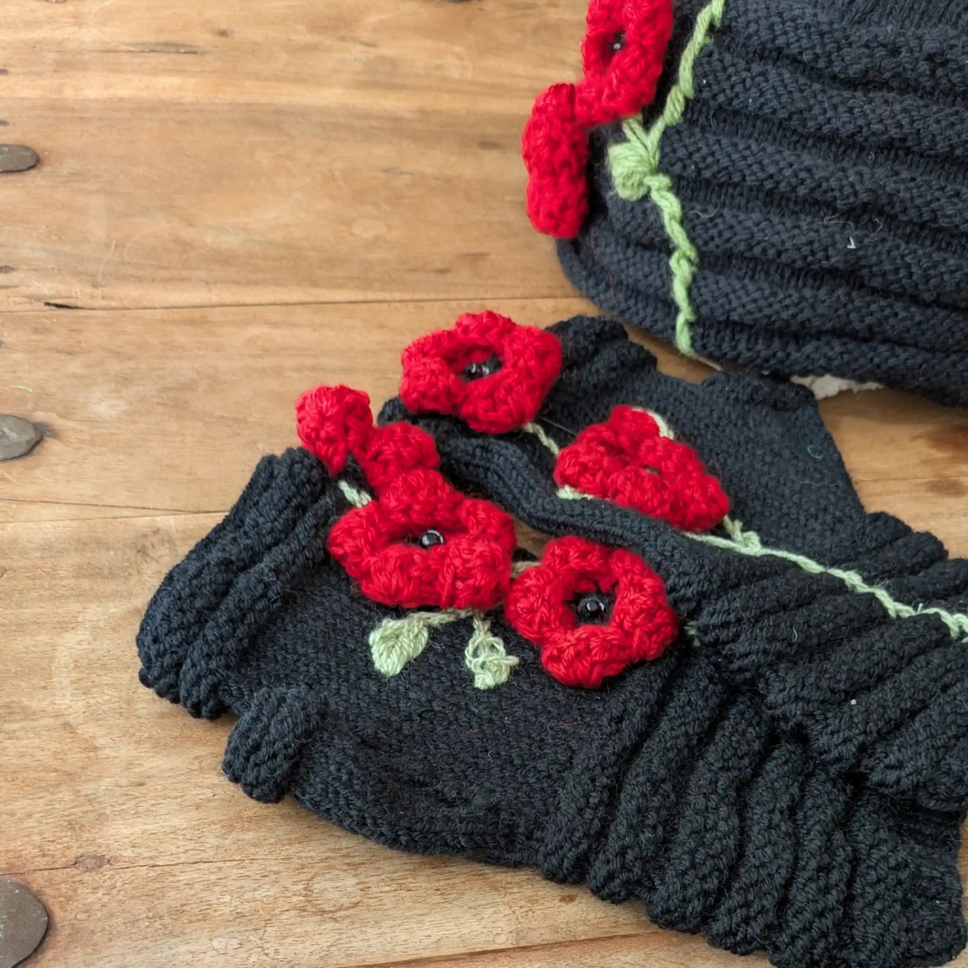 Détail des mitaines noires avec coquelicots rouges appliqués, tiges vert clair et maille en bourrelets.