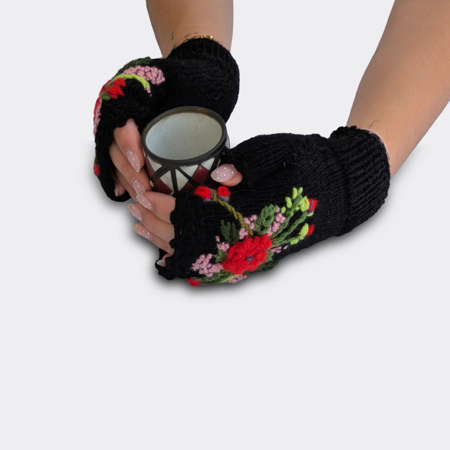 Mitaines femme noires portées avec une tasse entre les mains. Le décor rouge poudré associe fleurs appliquées, tiges brodées et touches rose pâle. La finition supérieure est festonnée.