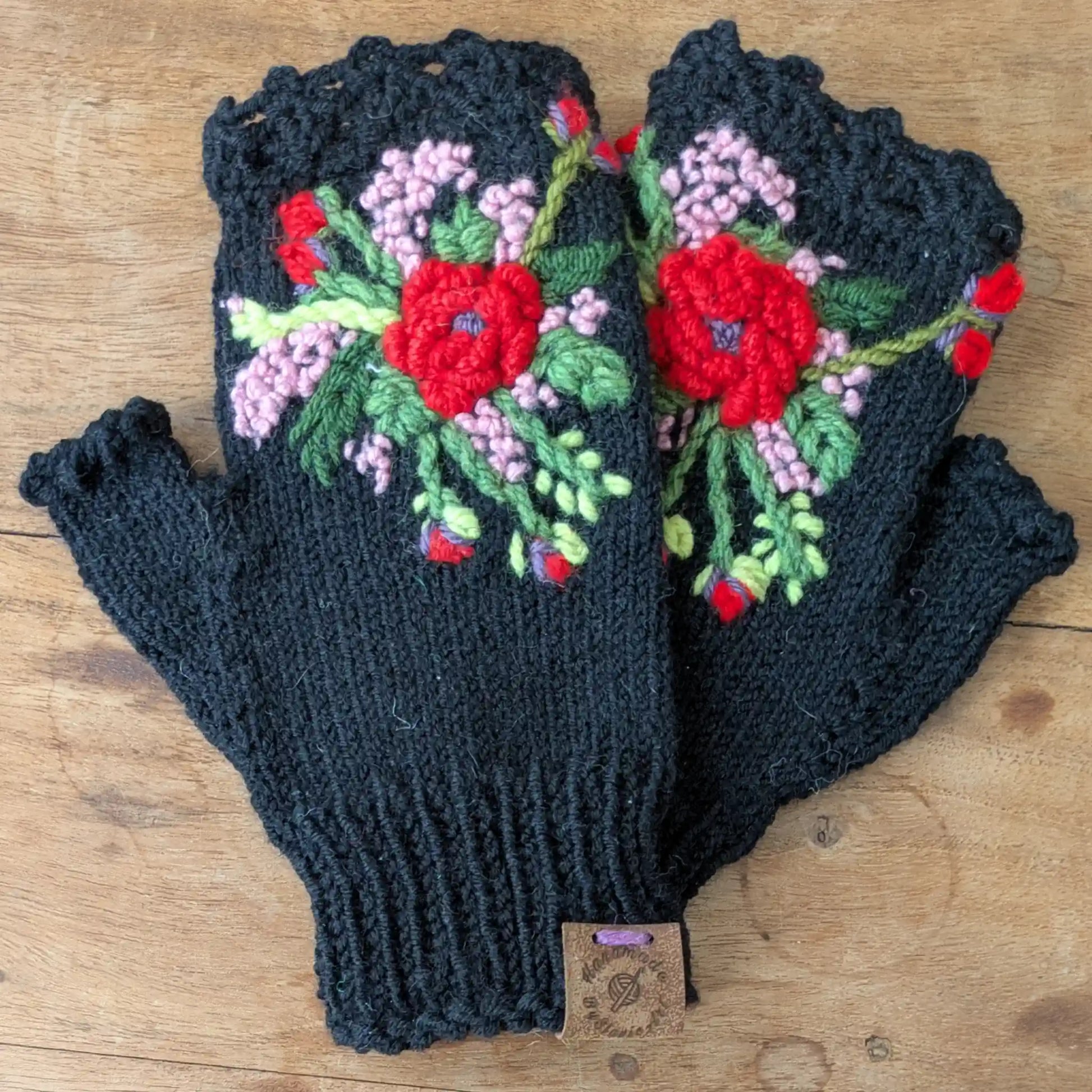Mitaines noires tricotées main avec décor floral rouge, rose pâle et vert sur le dessus.