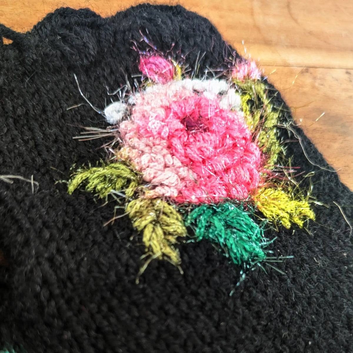 Gros plan d'une rose scintillante crochetée sur une paire de mitaines noire pour femme.