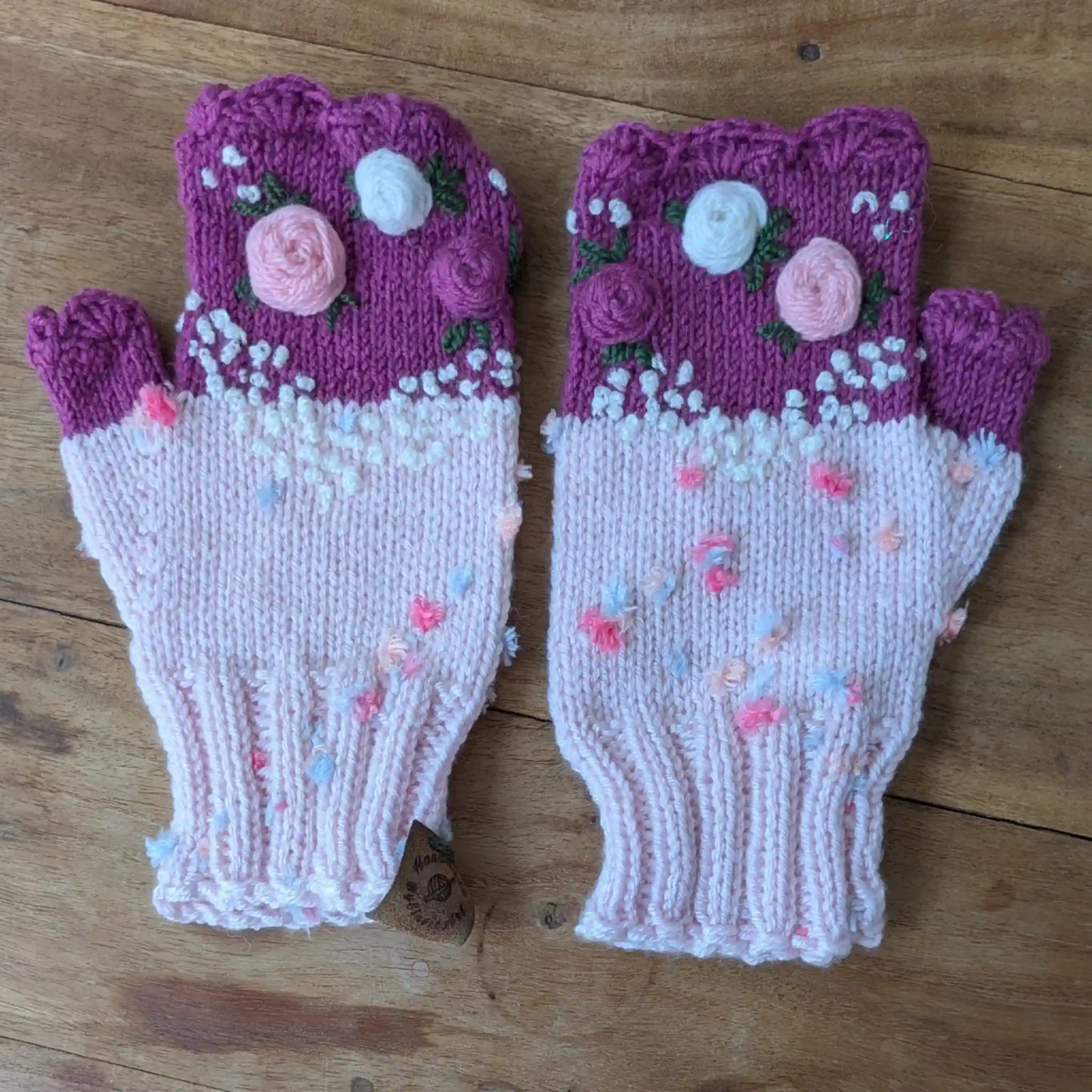 Mitaines roses faites main avec roses pastel appliquées, bord supérieur violet et broderies végétales.