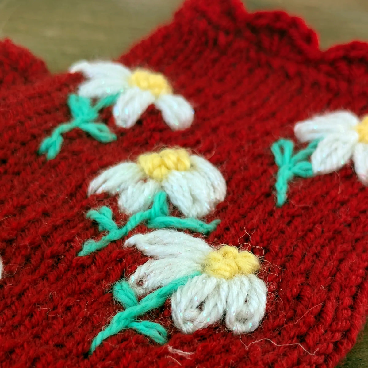 Détail de petites fleurs brodées sur une paire de mitaines rouges artisanales pour femme.