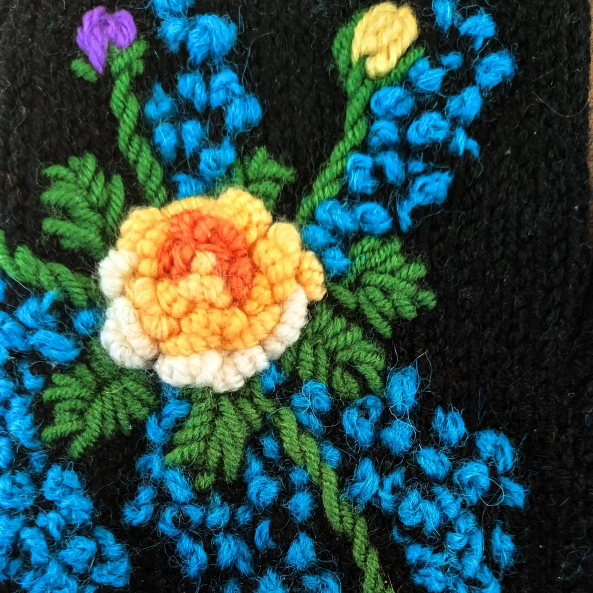 Vue en gros plan sur une paire de mitaine d'une fleur blanche, jaune et dorée entourée de petites fleurs bleues.