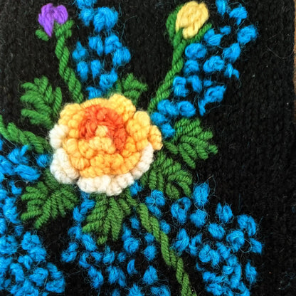 Vue en gros plan sur une paire de mitaine d'une fleur blanche, jaune et dorée entourée de petites fleurs bleues.