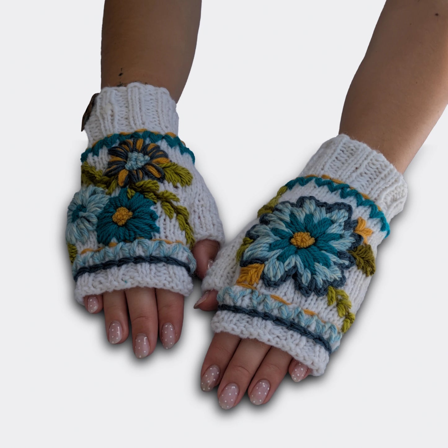 Mitaines tricotées main blanc cassé, portées à plat, décorées de fleurs bleues et turquoises avec feuillage brodé.