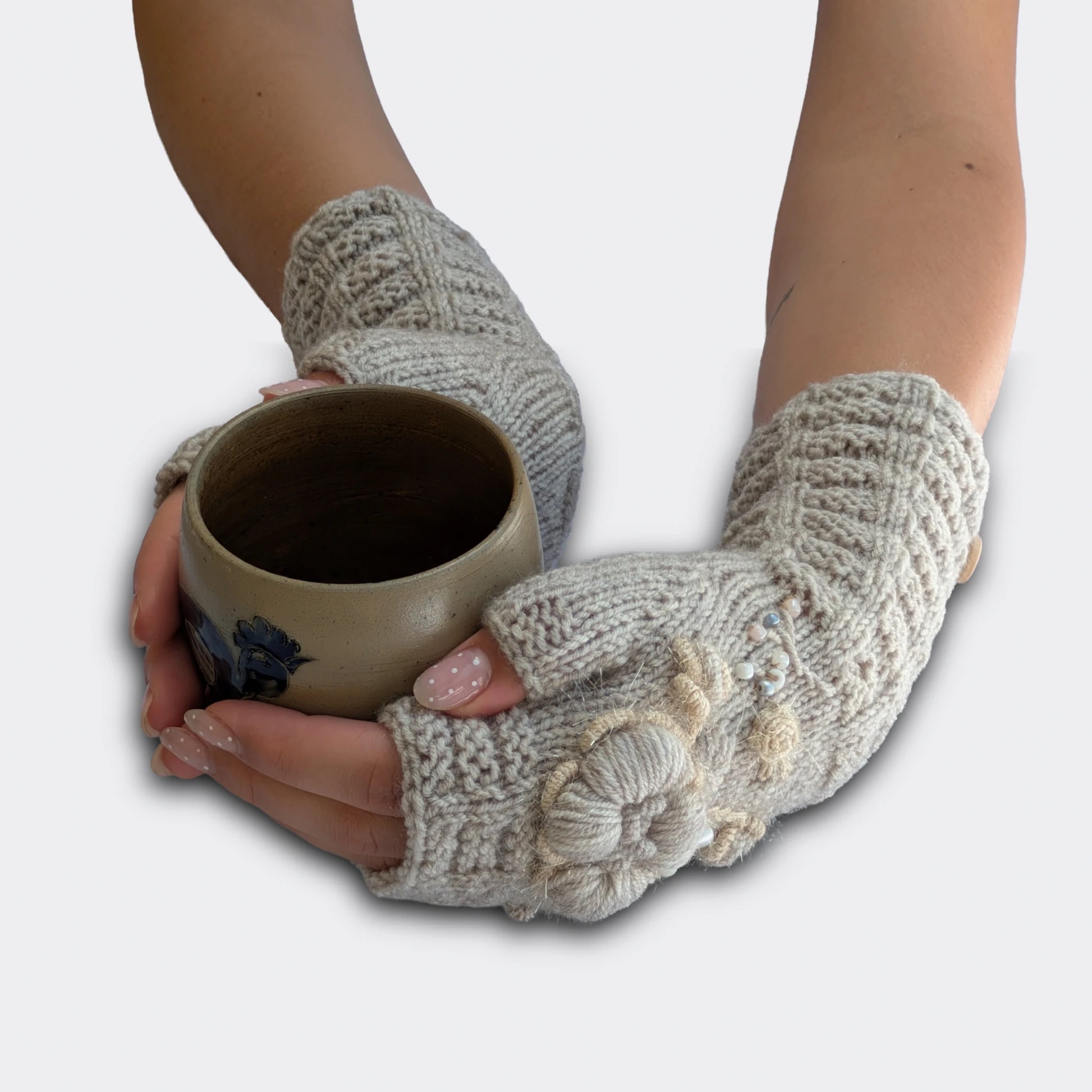 Mitaines gris clair tricotées main tenant une tasse, décorées de broderies florales beige-écru.
