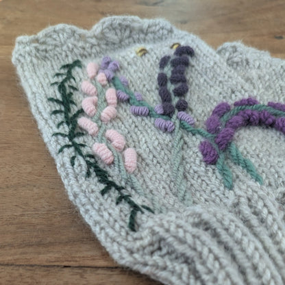Mitaines tricotées main, maille jersey, composition florale de type bruyère, couleurs parme, violet et rose pâle. Vue latérale gauche.