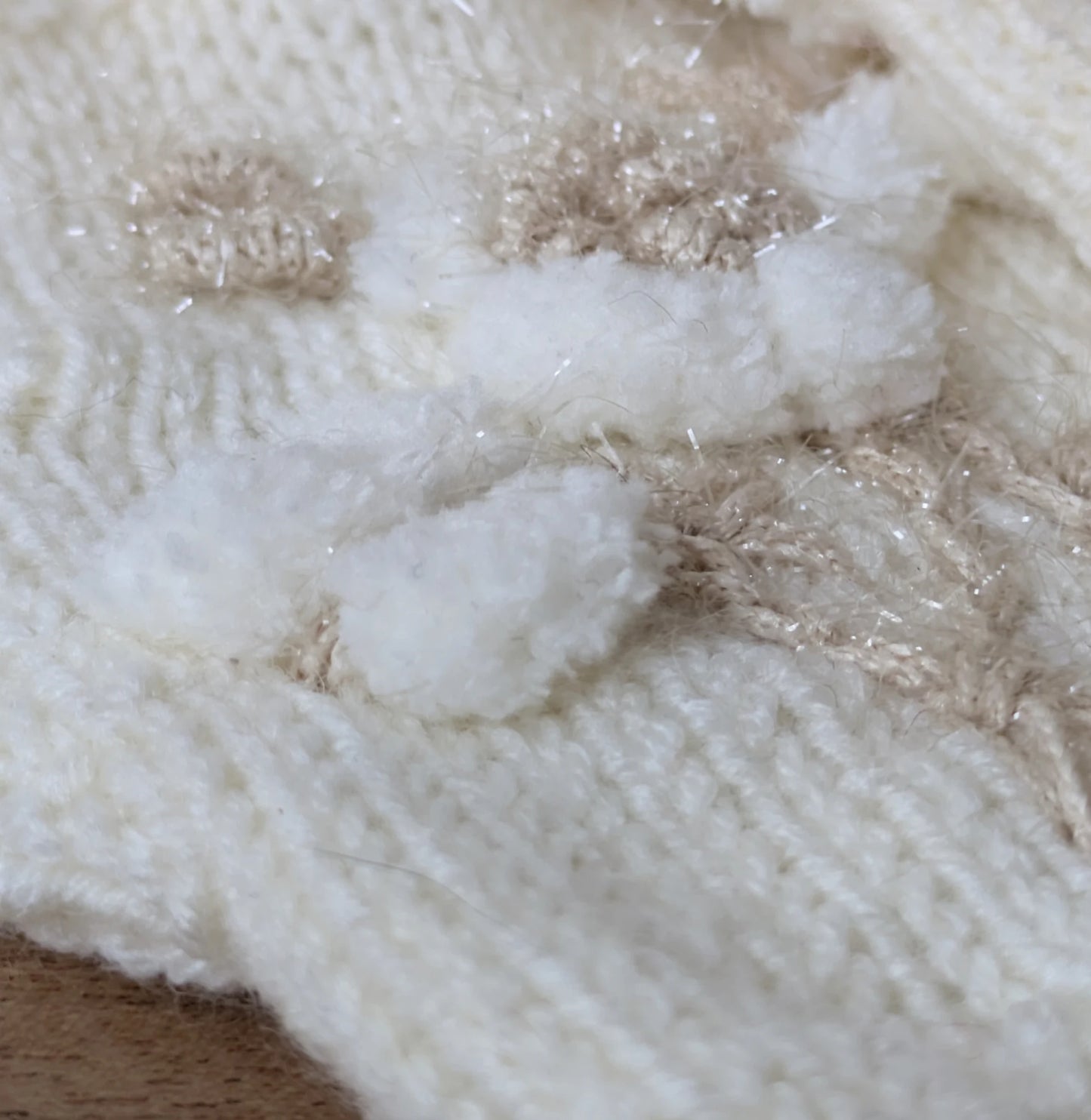 Gros plan sur la fleur blanche en relief et les petites boules appliquées sur les mitaines.
