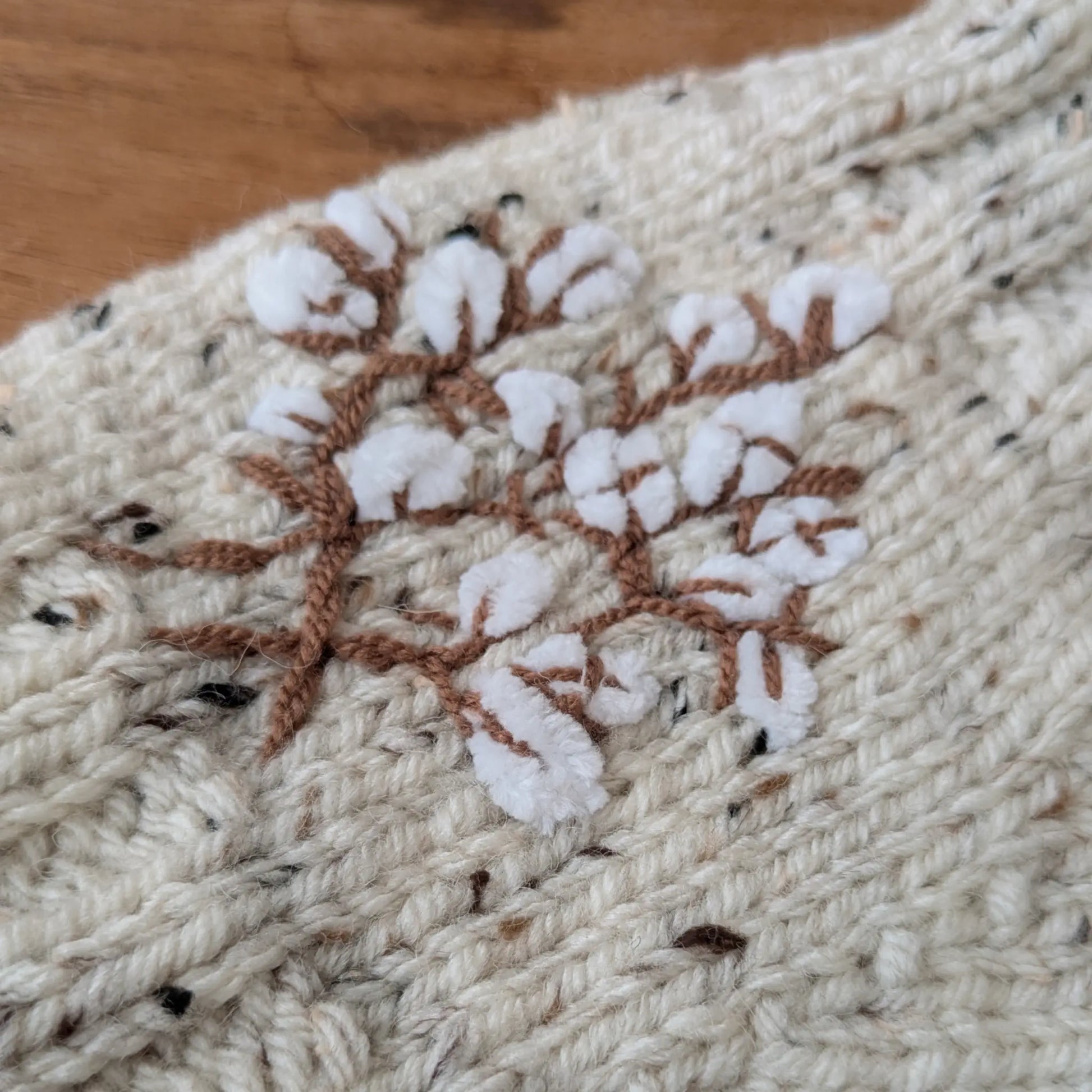 Détail des branches de coton stylisées brodées sur la maille écru mouchetée des mitaines.