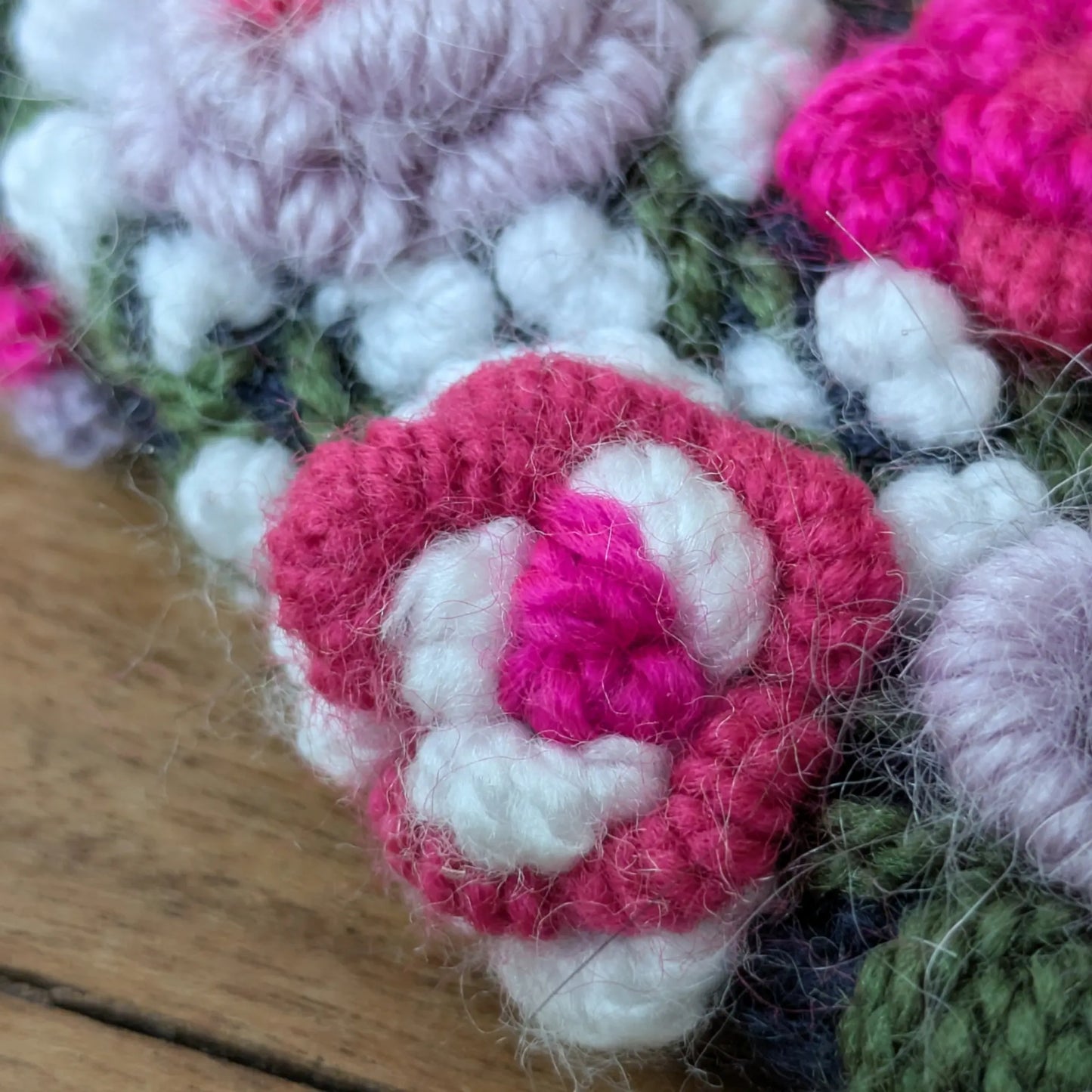 Détail des roses crochetées roses et blanches sur des mitaines bleu nuit faites main.