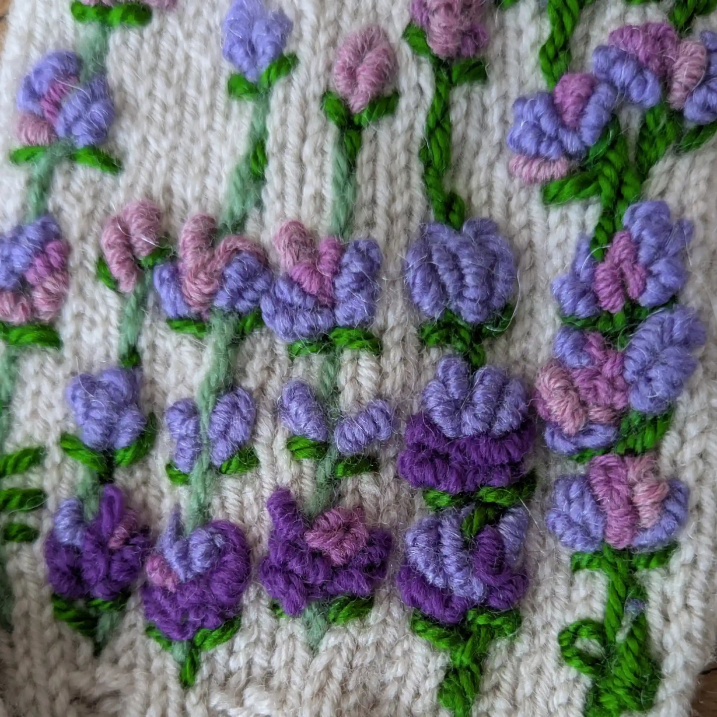 Détail des fleurs violettes et mauves brodées sur la maille gris clair des mitaines.
