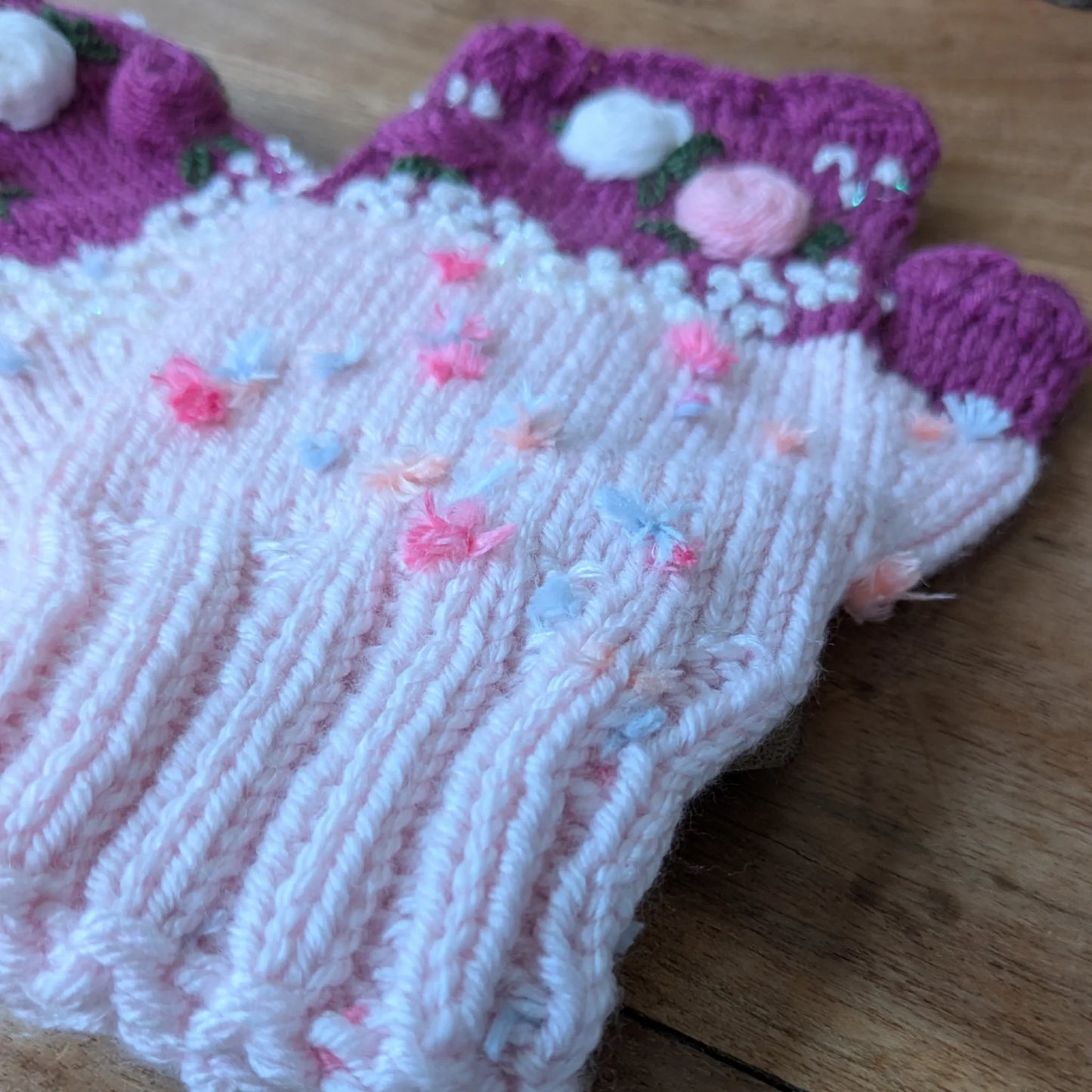 Détail de la maille rose clair, des petites broderies roses et du bord festonné des mitaines.