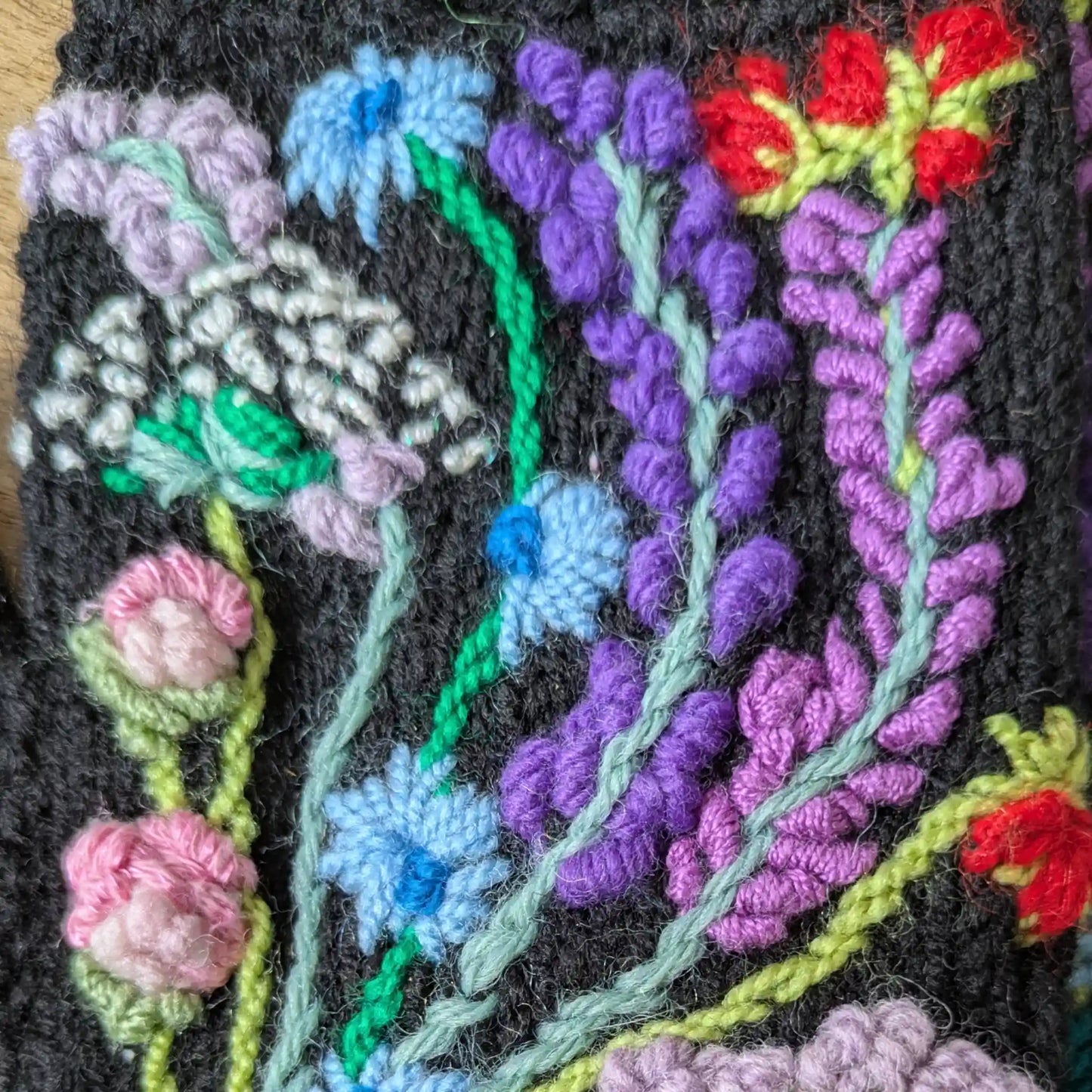 Détail des fleurs brodées rose, turquoise, vert et rouge sur des mitaines noires.