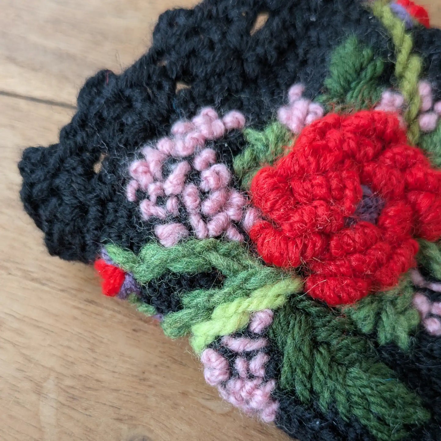 Détail du décor floral rouge, rose pâle et vert brodé sur des mitaines noires.