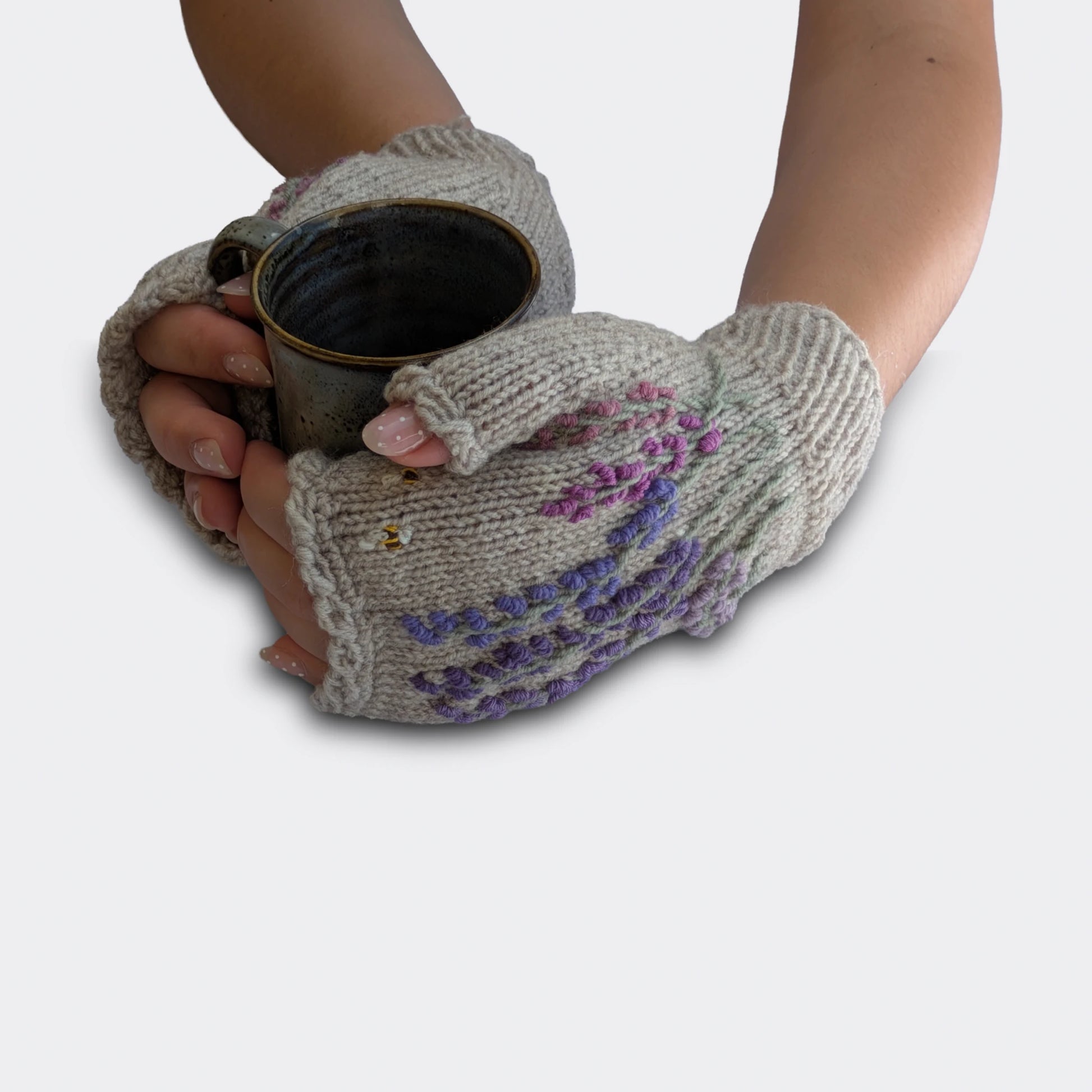 Mitaines gris perle tenant une tasse, décorées de lavandes brodées mauves, petites abeilles et bord côtelé au poignet.