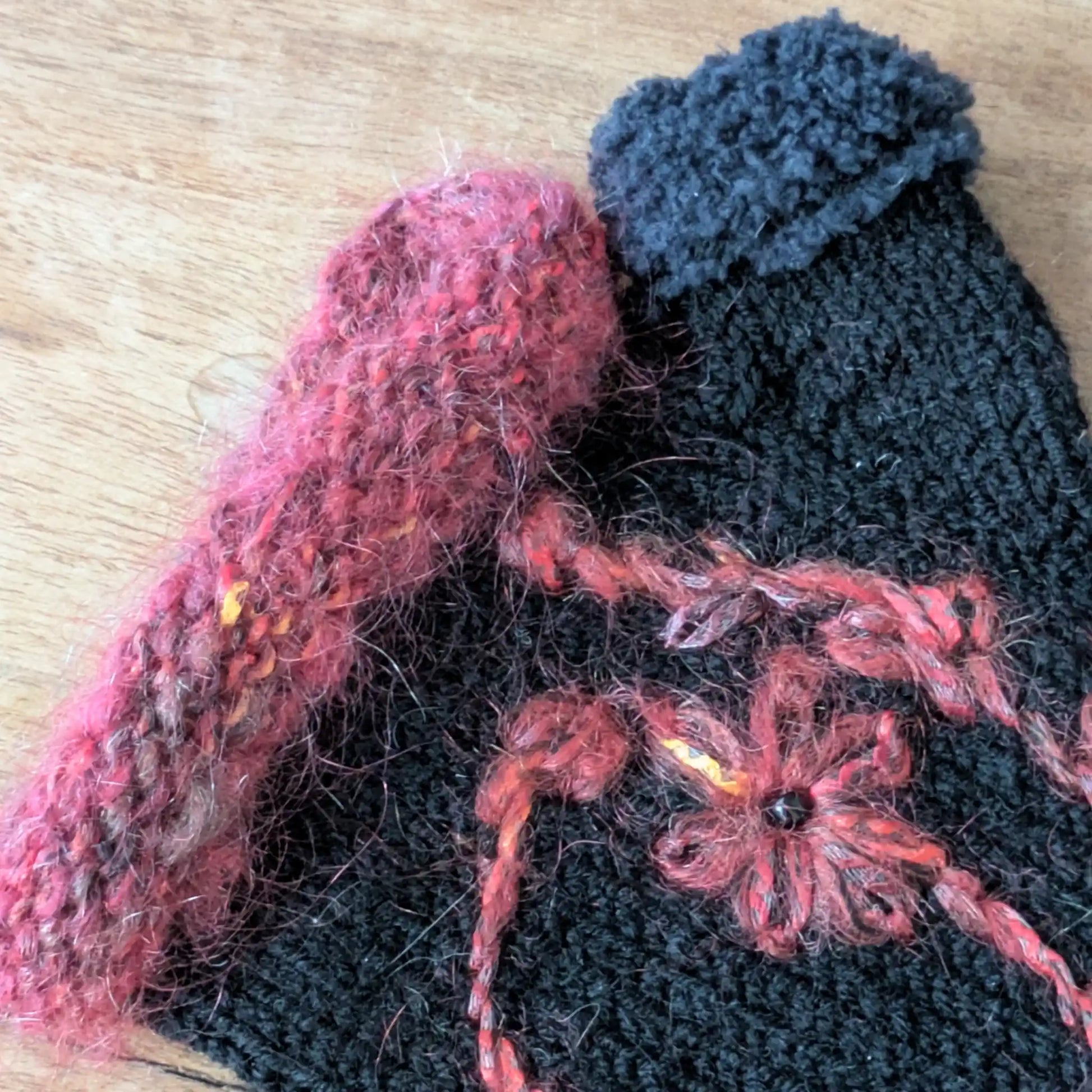Détail de l’ourlet supérieur couleur rouille (couleur bleue sur le pouce) et du motif floral sur des mitaines artisanales noires.