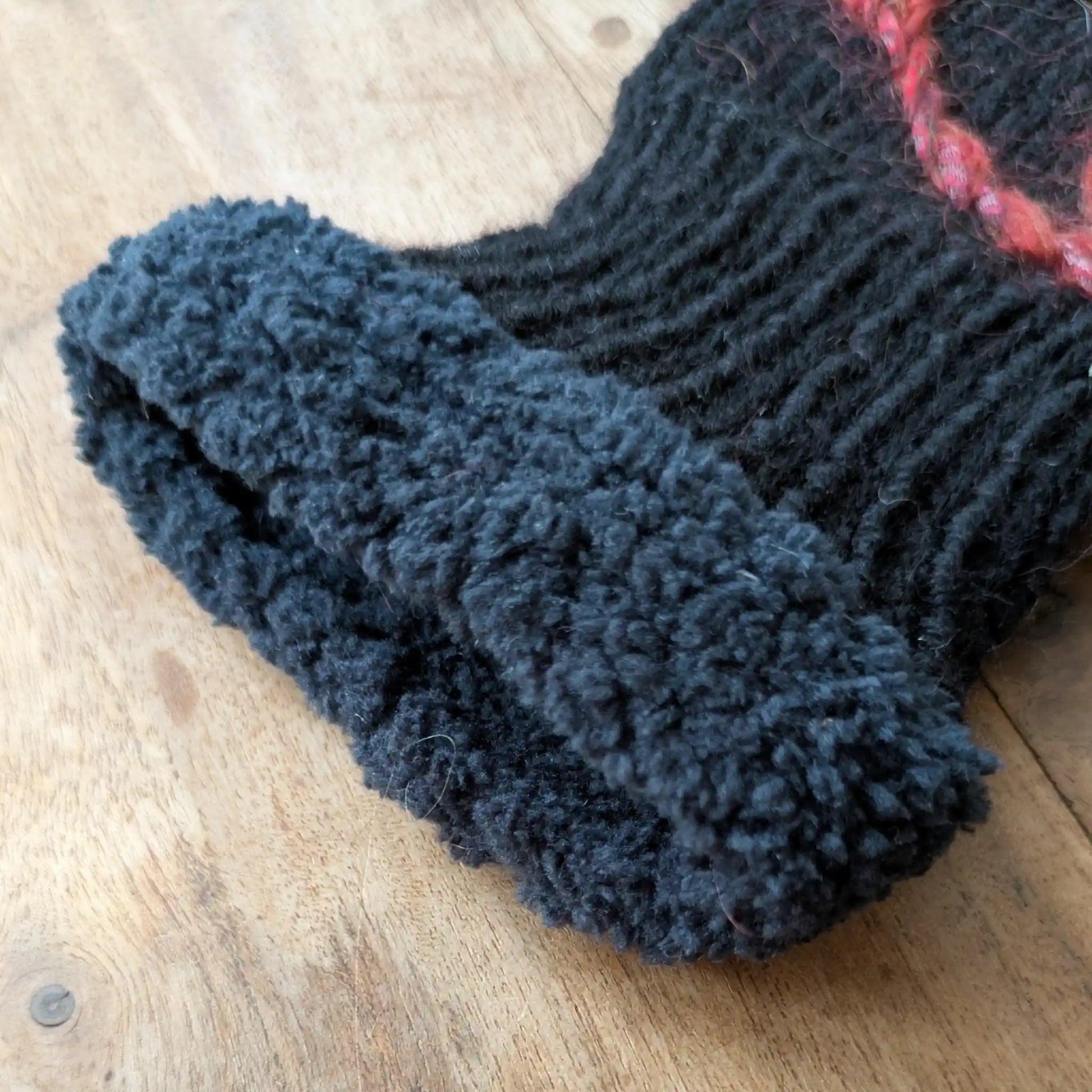 Gros plan sur le bord  bleu profond au poignet des mitaines noires tricotées main.