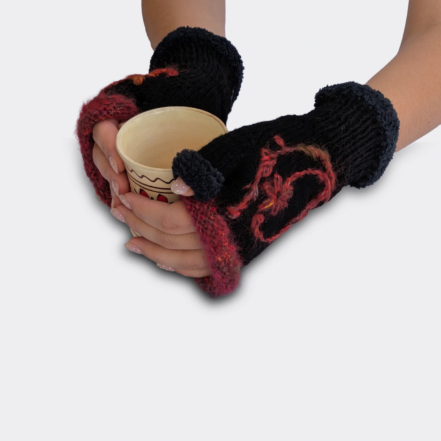 Mitaines noires brodées tenant une tasse, avec fleur rouille en relief, feuillage vert et bord supérieur replié.
