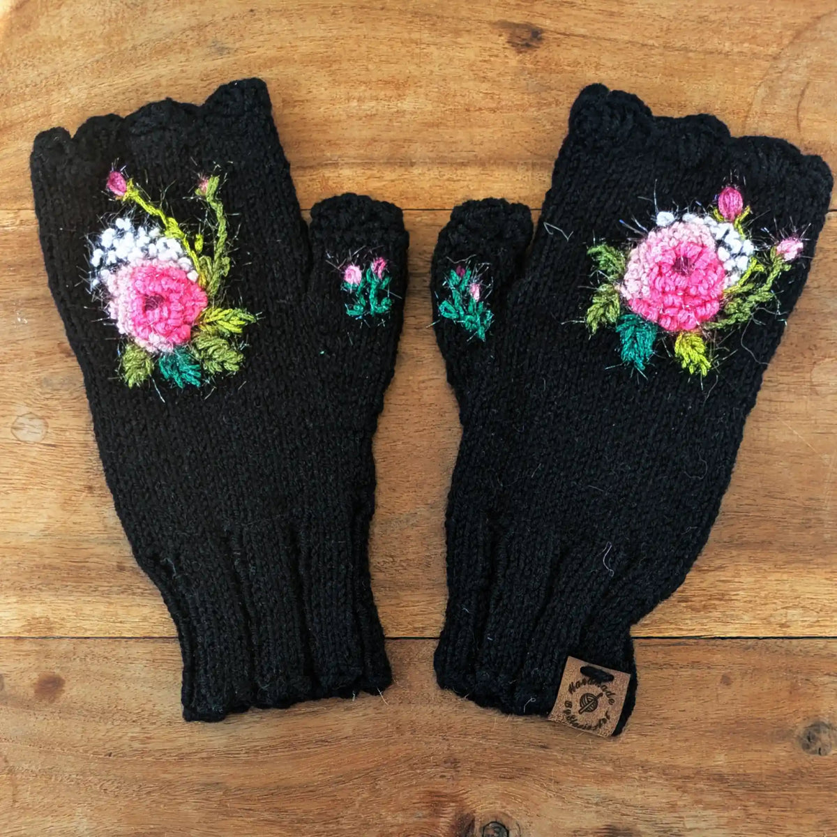 Paire de mitaines noires présentées à plat sur une table. Elles sont ornées d'une composition florale : une rose scintillante entourées de petits points blancs.