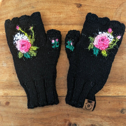 Paire de mitaines noires présentées à plat sur une table. Elles sont ornées d'une composition florale : une rose scintillante entourées de petits points blancs.
