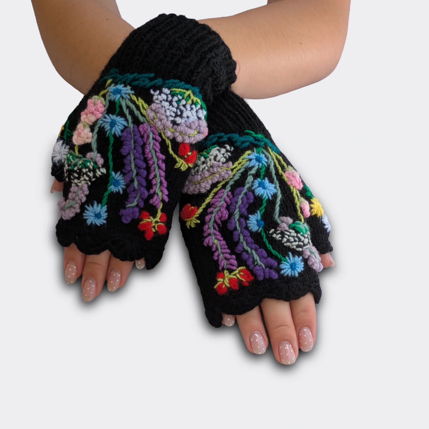 Mitaines noires portées mains croisées, avec fleurs multicolores brodées et décor floral en relief.