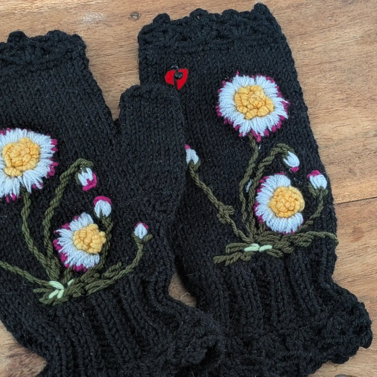 Paire de mitaines noires festonnées, tricotées main, avec des pâquerettes crochetées puis brodées sur le dessus.