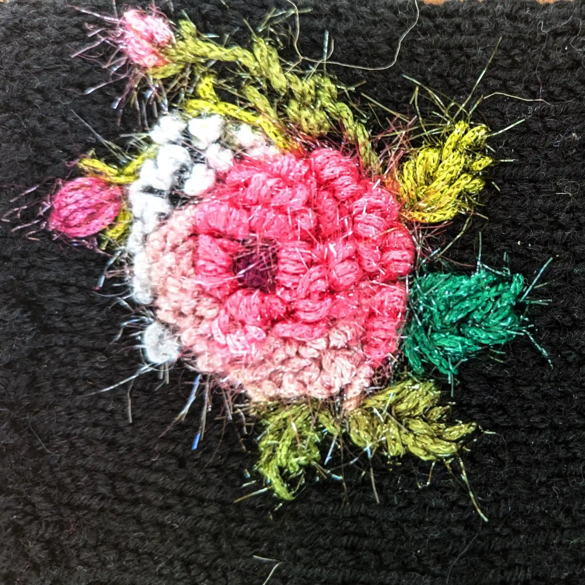Vue du dessus de la composition florale d'une paire de mitaines noires pour femme. On y distingue une rose entourée de tiges et de deux boutons de rose.