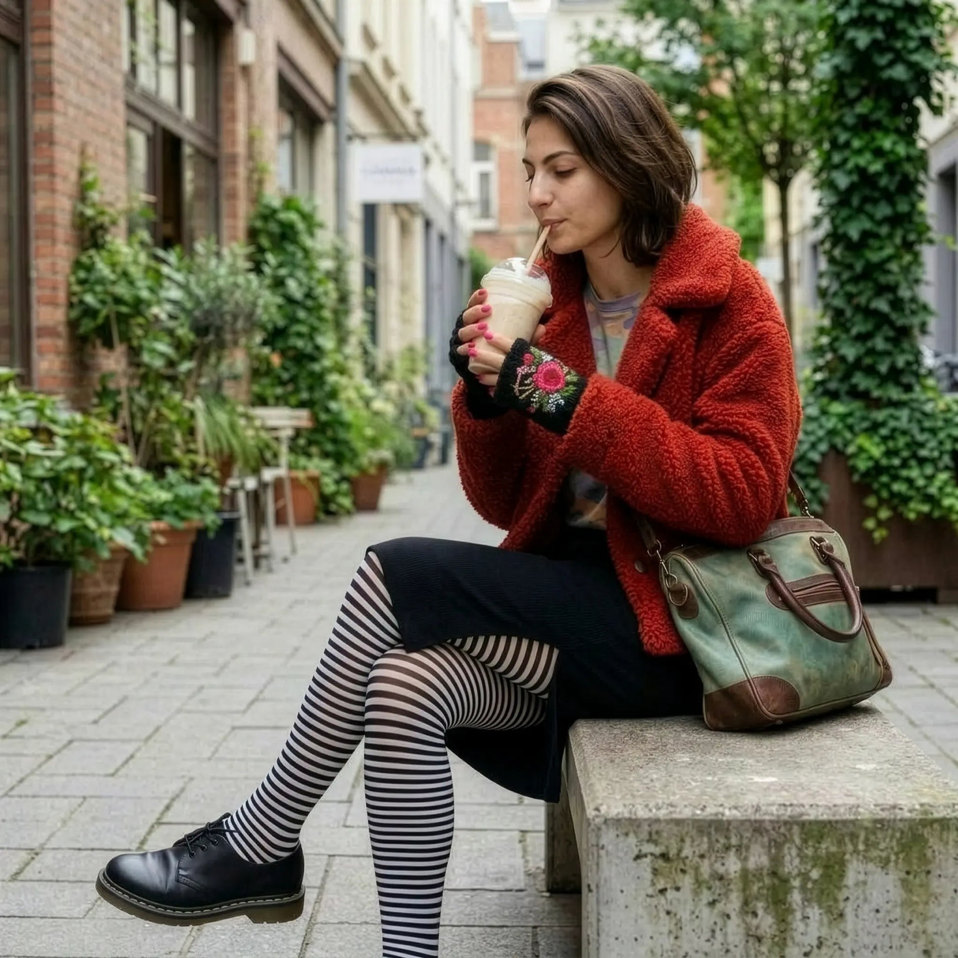 Mitaines brodées noires portées dans une scène urbaine, avec veste rouge, collants rayés et motif floral rose en relief.
