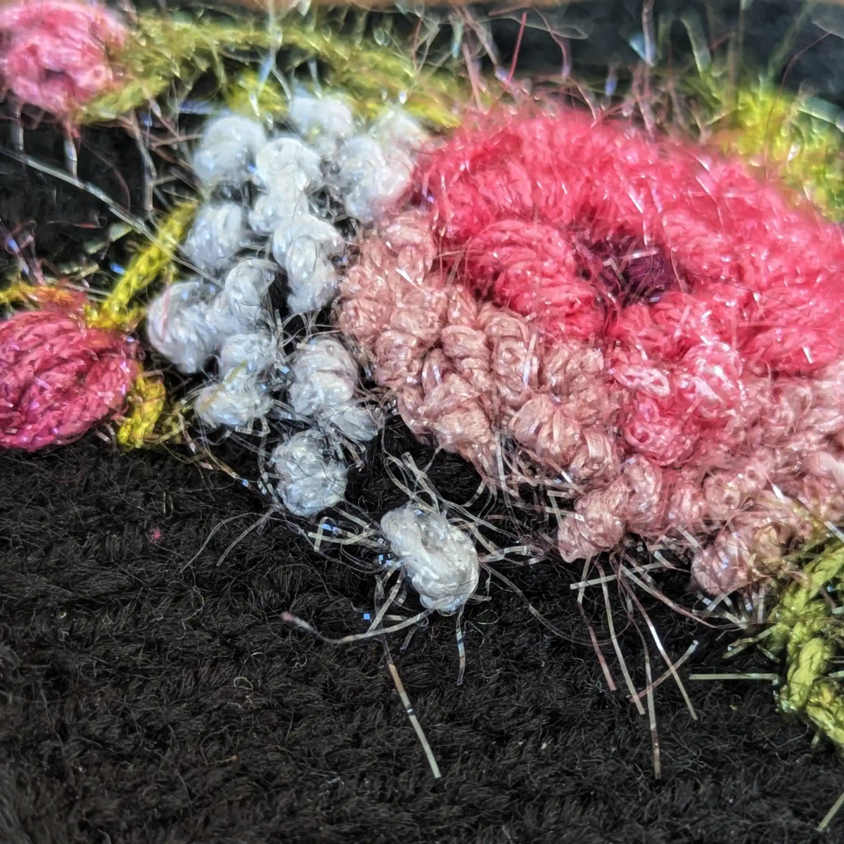 Vue en détail et latérale d'une rose crochetées et brodée sur une paire de mitaines noires artisanales.