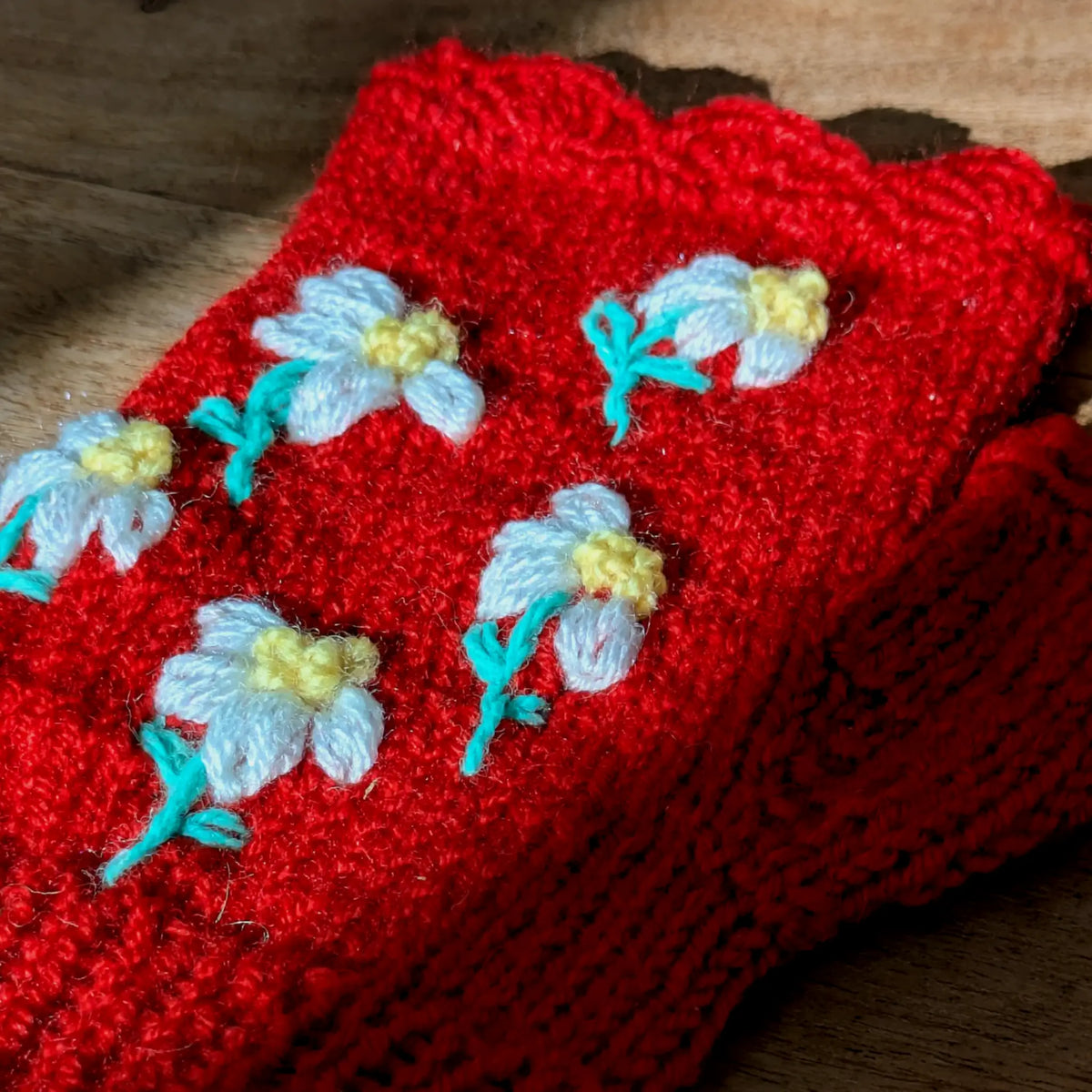 Vue supérieure d'une paire de mitaines rouges exposée à plat sur une table où passe un rai de lumière ensoleillé. De petites fleurs très mignonnes ornent le dessus.