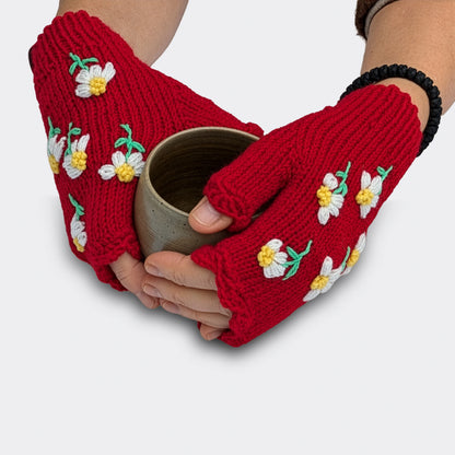 Mitaines pour femme tricotées main, portées sur des mains tenant une tasse. Les fleurettes blanches sont disposées en semis sur fond rouge, avec une finition festonnée en haut.
