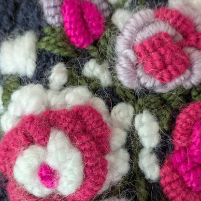 Gros plan sur les fleurs blanches et roses appliquées sur la maille bleu nuit des mitaines.