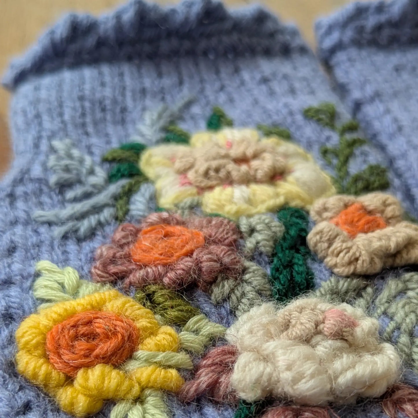 Gros plan sur les fleurs jaunes, crème et pêche en relief de ces mitaines bleu lavande tricotées main.