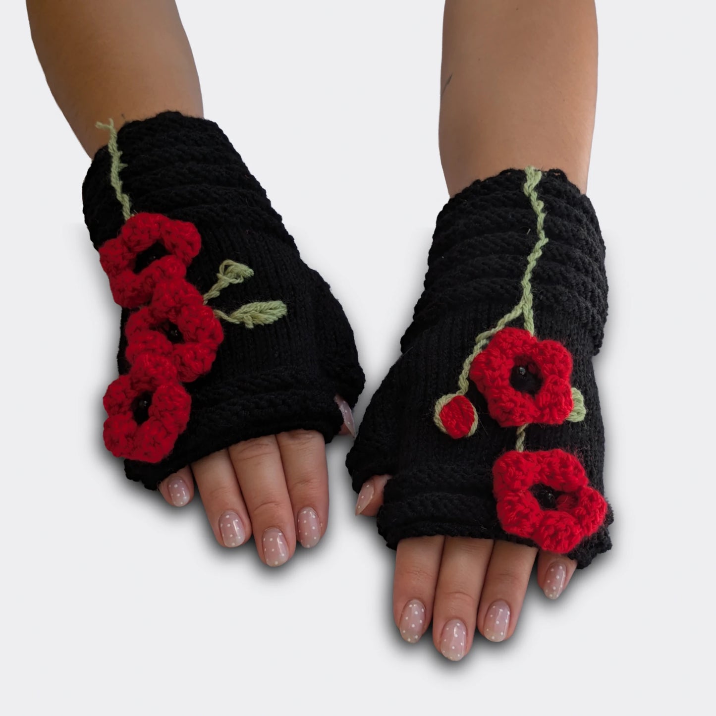 Mitaines tricotées main sur fond noir, portées à plat, avec coquelicots rouges crochetés et perles noires au centre des fleurs.