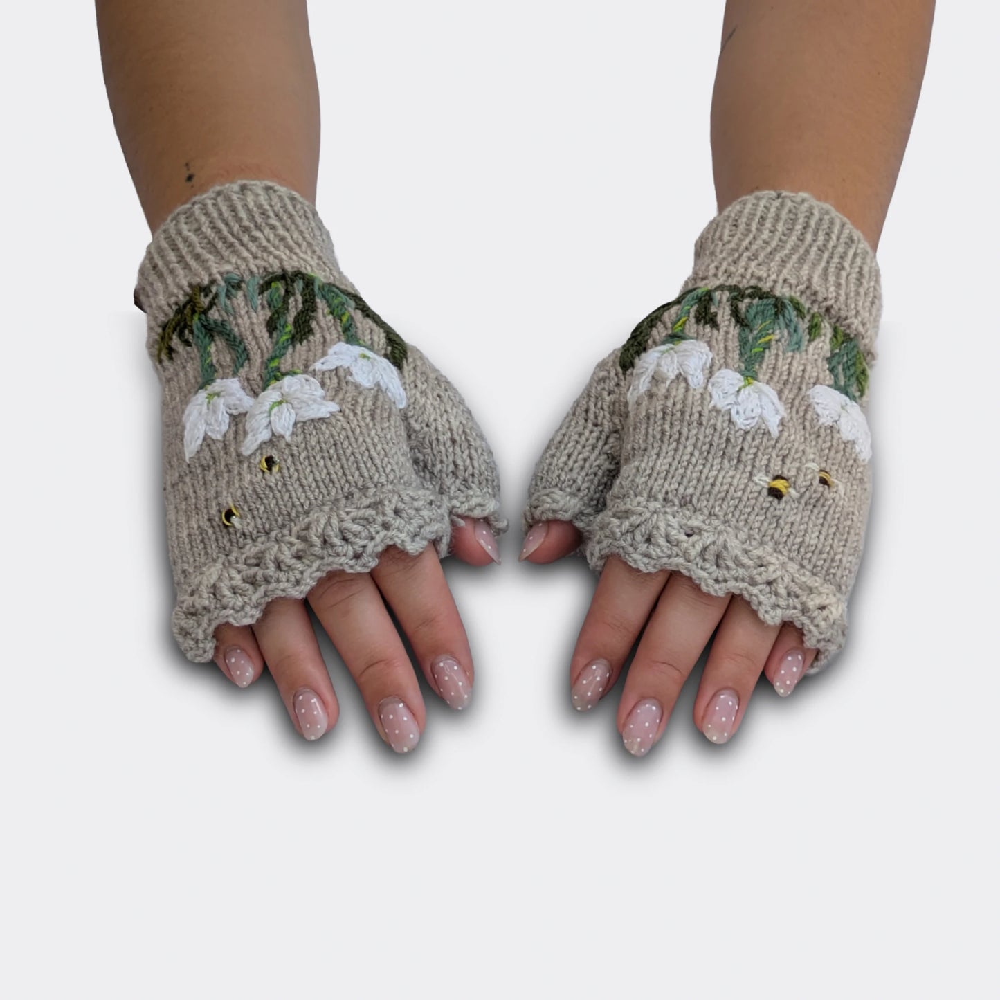 Mitaines tricotées main gris perle portées à plat, avec crocus blancs crochetés puis brodés et feuillage vert.