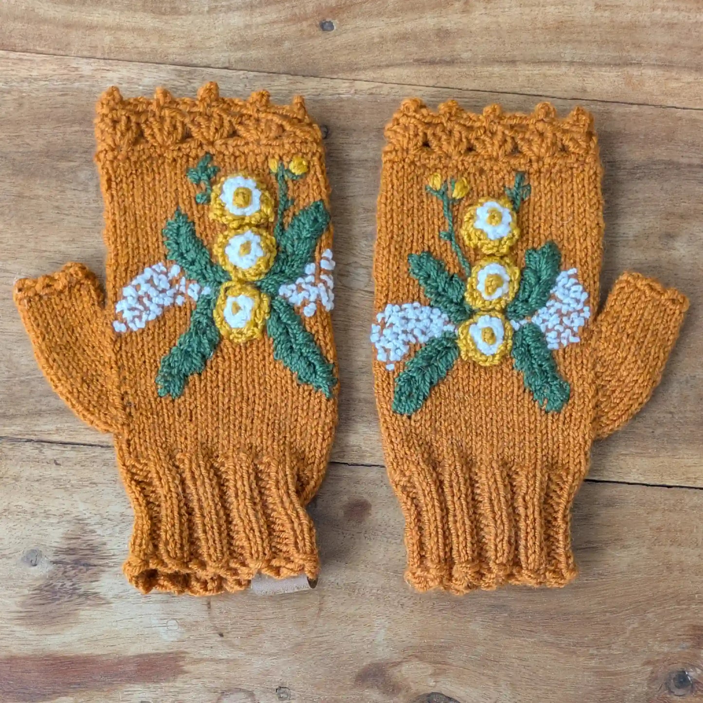 Mitaines couleur cuivre posées à plat, avec fleurs jaunes et blanches crochetées et broderies florales.