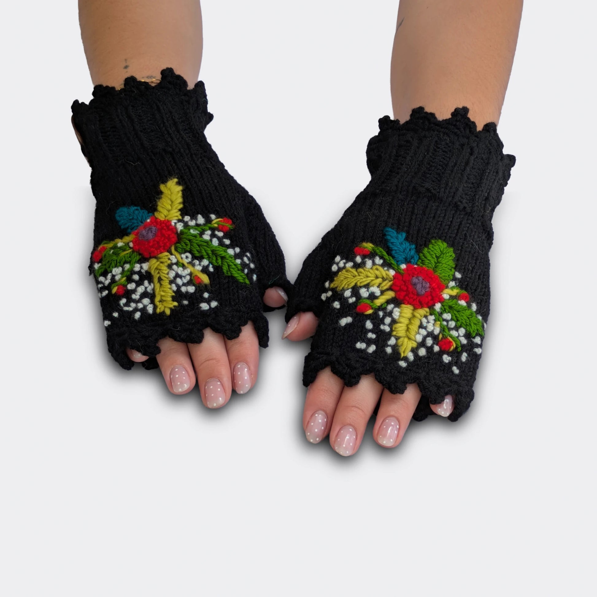 Mitaines tricotées main sur fond noir, portées à plat, avec fleurs multicolores appliquées, feuillage brodé et bord festonné.
