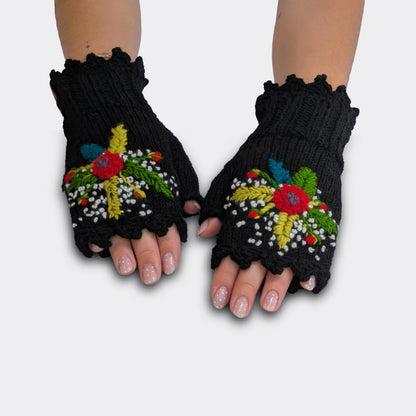 Mitaines tricotées main sur fond noir, portées à plat, avec fleurs multicolores appliquées, feuillage brodé et bord festonné.