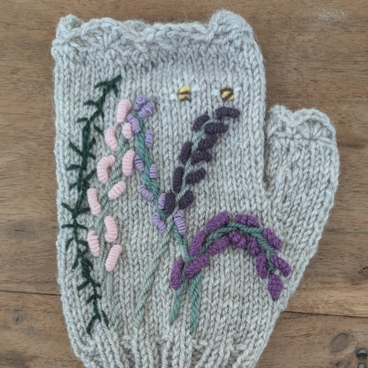 Vue du dessus d'une mitaine grise pour femmes où un décor floral parme et violet évoquant les landes se dessine. Tricoté à la main.