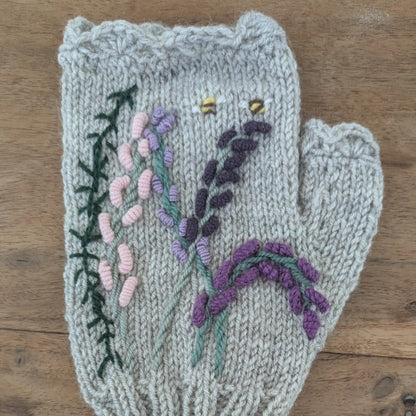 Vue du dessus d'une mitaine grise pour femmes où un décor floral parme et violet évoquant les landes se dessine. Tricoté à la main.