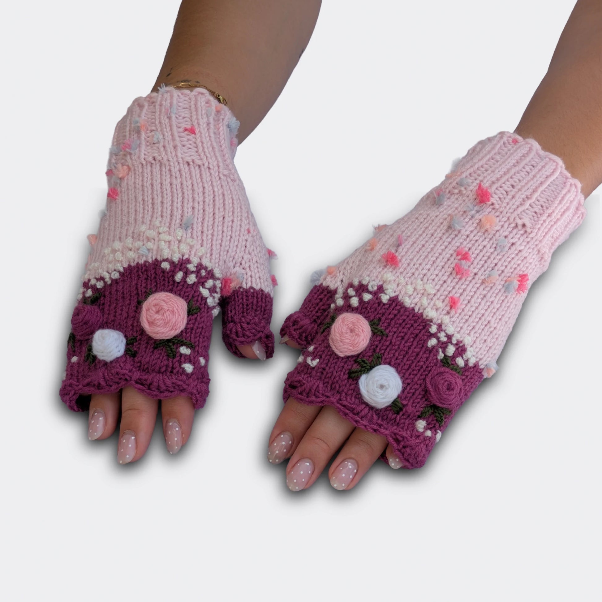 Mitaines tricotées main rose clair et vieux rose, portées à plat, avec fleurs pastel appliquées et fines broderies végétales.