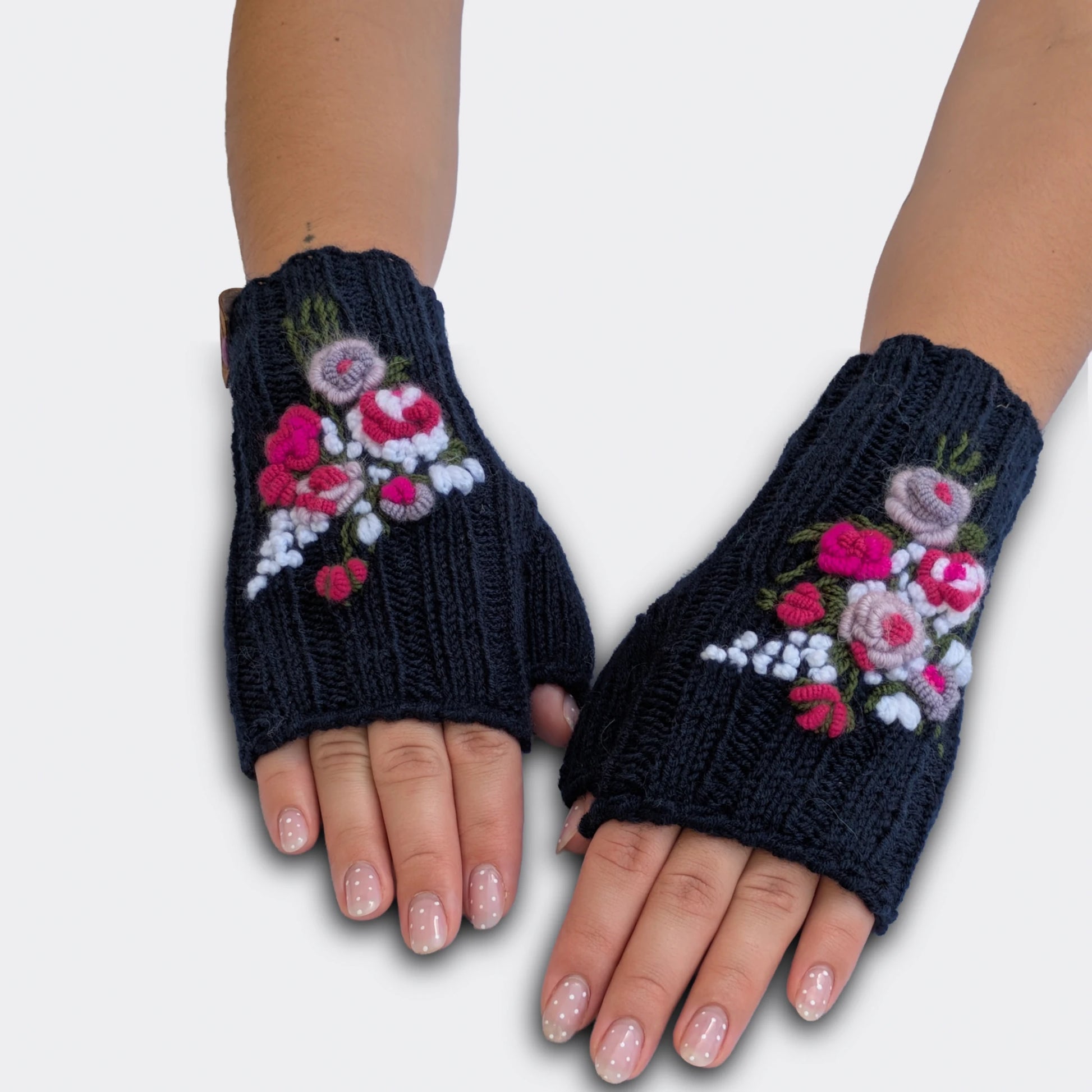 Vue à plat de mitaines artisanales bleu nuit. Les roses anciennes rose pâle et fuchsia sont appliquées en relief sur la maille côtelée. De petites fleurs blanches et des tiges vertes complètent le décor.