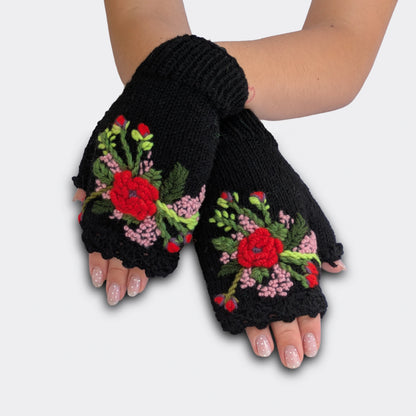 Mitaines faites main en Serbie, portées mains croisées. Les fleurs appliquées ressortent sur le fond noir, avec une nuance rouge poudré et des broderies végétales. Le haut des mitaines est festonné.