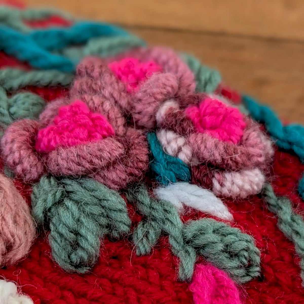 Zoom sur la composition florale de mitaines femme rouges. Les couleurs des fleurs sont multiples : mauves, roses, la tige est verte.