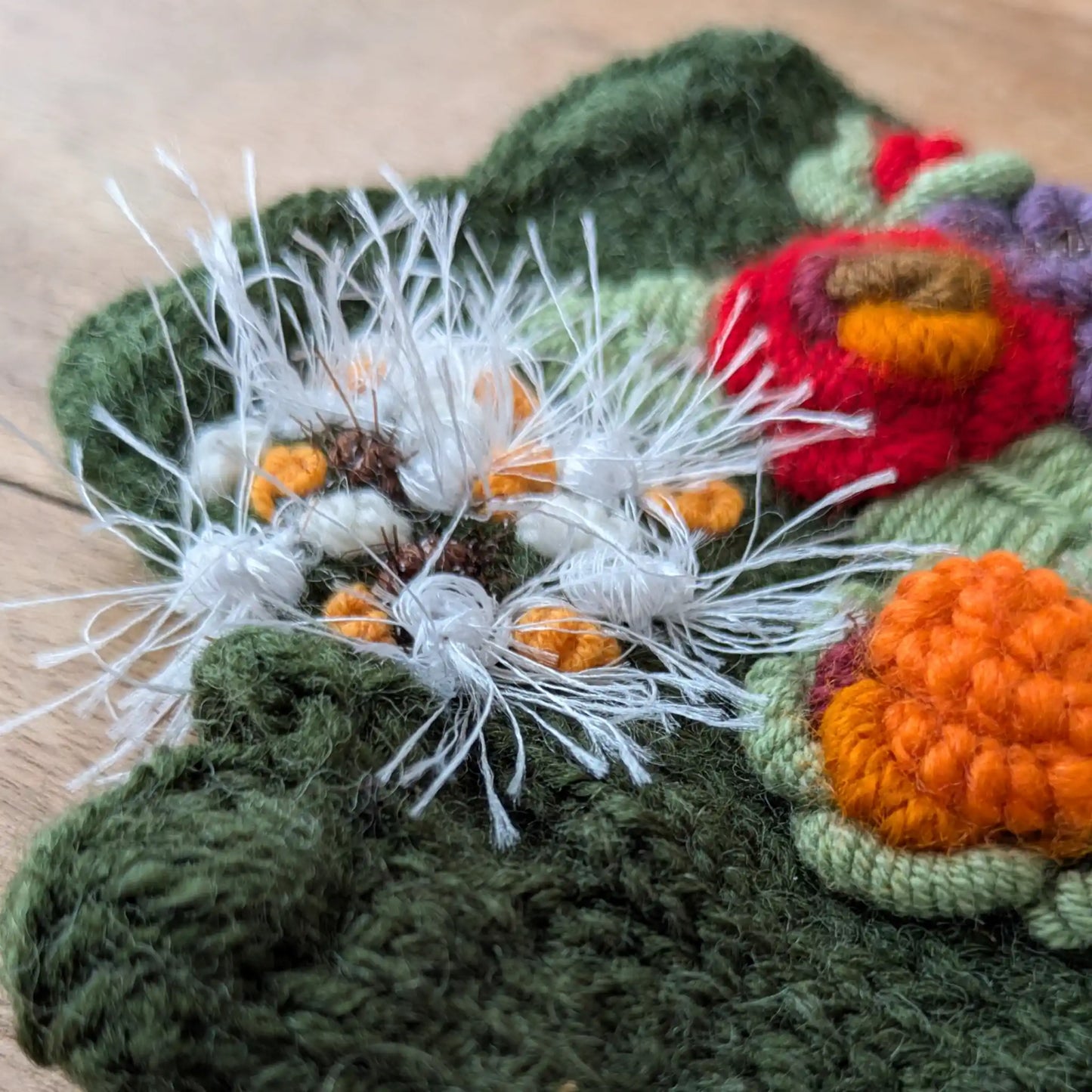 Gros plan sur les fleurs appliquées et les broderies de feuillage de ces mitaines tricotées main vert olive.